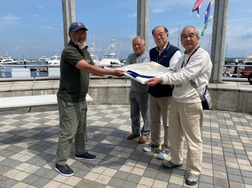 横浜ベイサイドマリーナで、江口艇長（左）からフラッグを受け取る貝道会長（右から3番目）、足立会長（右端）
